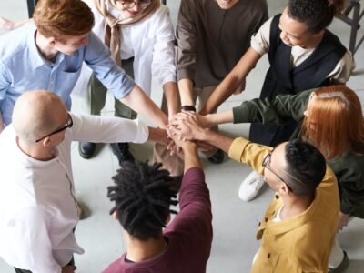 team of 8 people standing in a circle reaching out a hand to connect with others in the centre