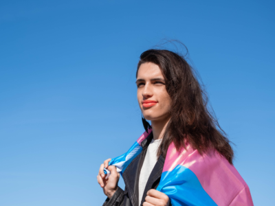 smiling person with the transgender flag draped over their shoulders