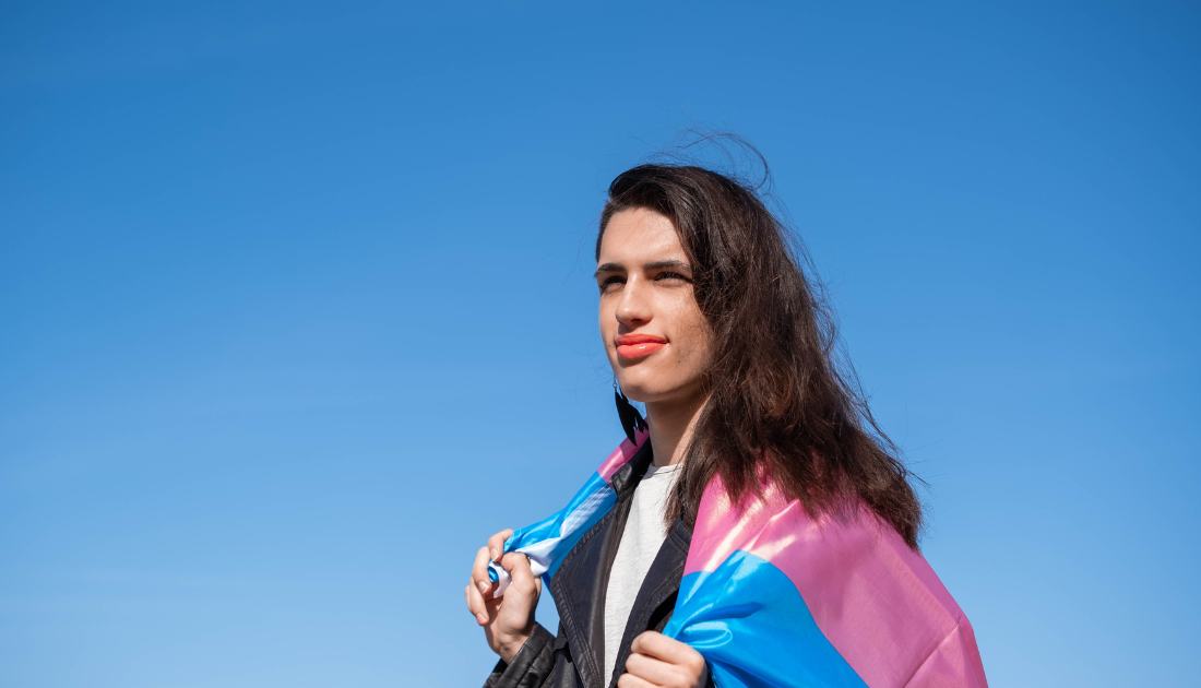 smiling person with the transgender flag draped over their shoulders